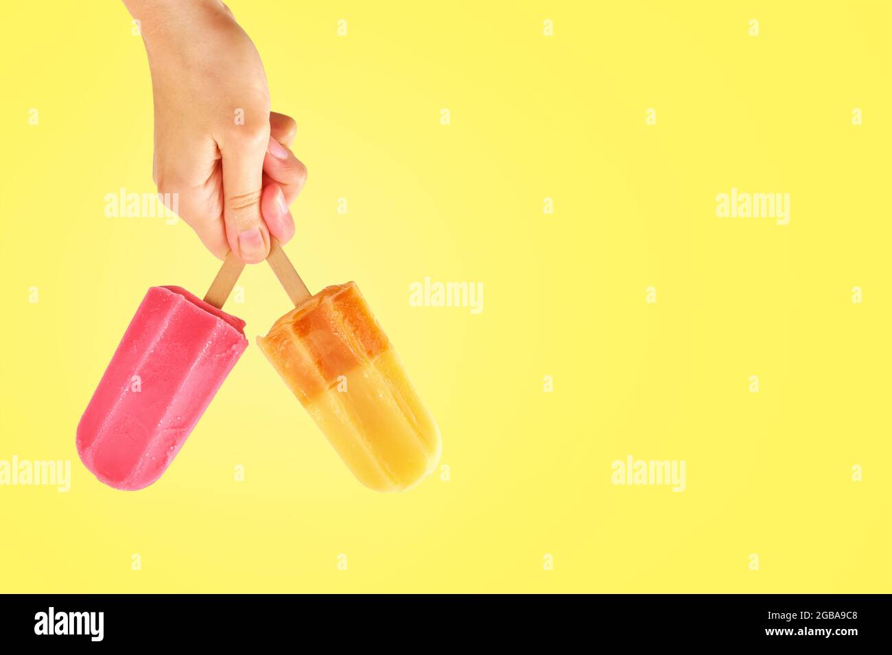 Buntes Eis in Frauenhand auf gelbem Hintergrund mit Kopierraum. Sommerhintergrund Stockfoto