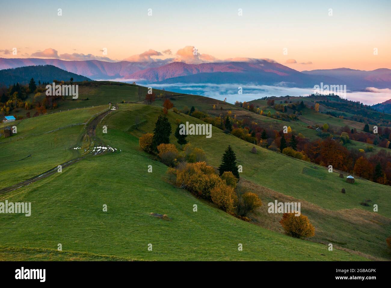 Bergige Landschaft im Herbst bei Sonnenaufgang. Wunderschöne Landschaft mit ländlichen Feldern auf Hügeln, die in das ferne Tal voller Nebel einrollen. Wolken darüber Stockfoto