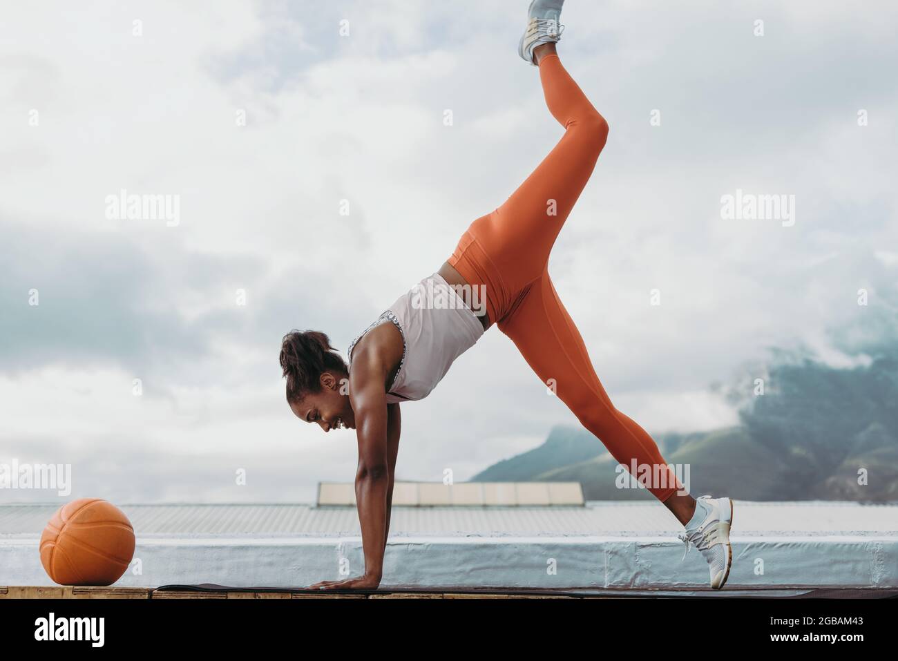 Frau in Sportkleidung mit Medizinball vor tun Stretching Yoga-Training im Freien. Die Sportlerin balanciert ihren Körper auf den Händen auf dem Dach. Stockfoto