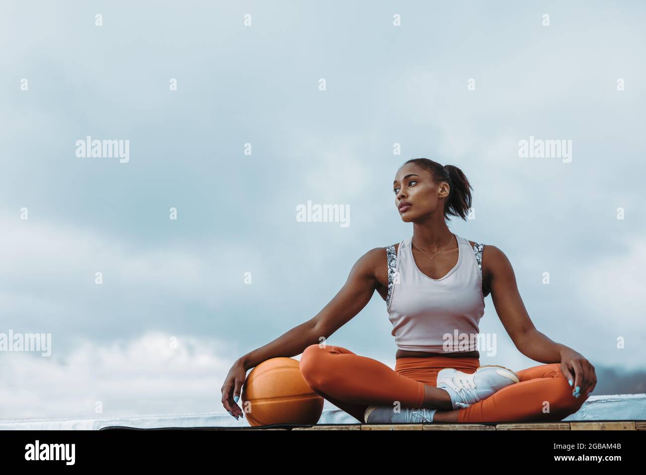 Schöne Frau in Sportkleidung sitzt mit Medizinball im Freien. Sportlerin, die sich nach dem Training auf der Terrasse entspannt. Stockfoto