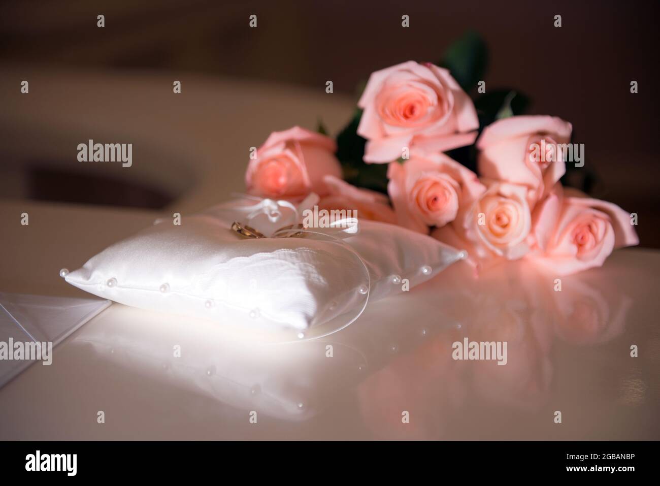 Goldene Eheringe auf einem weißen Pad in der Nähe von rosa Rosen-Bouquet Stockfoto