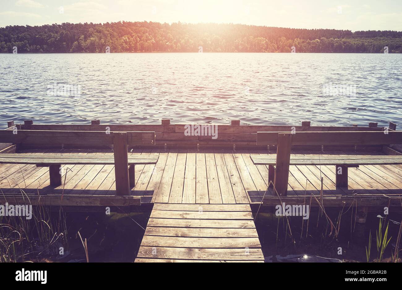 Holzsteg mit Bänken am See gegen die Sonne, Farbtonung aufgetragen. Stockfoto