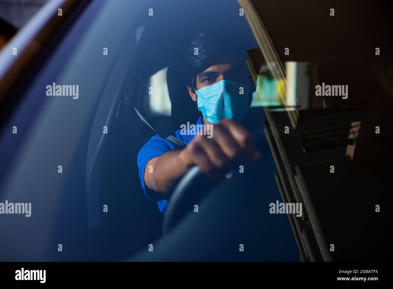 Ein junger Mann, der mit Gesichtsmaske in seinem Auto sitzt. Stockfoto