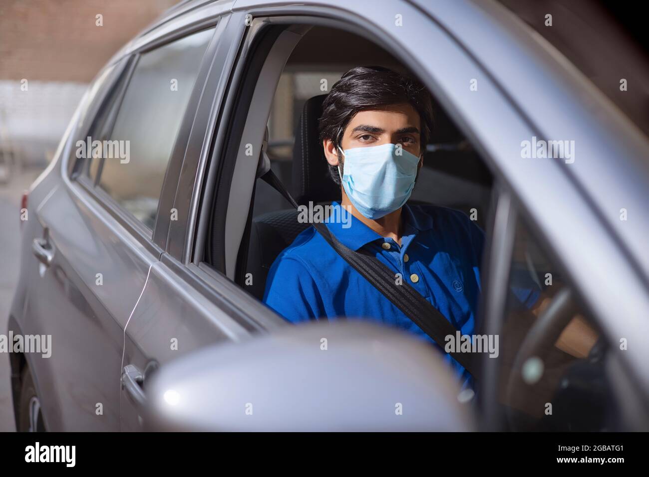 Ein junger Mann, der mit Gesichtsmaske in seinem Auto sitzt. Stockfoto