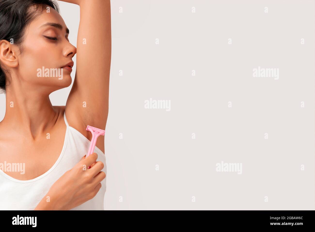 Eine junge Frau, die Haarentfernungsrasierer auf ihren Achselhöhlen verwendet. Stockfoto