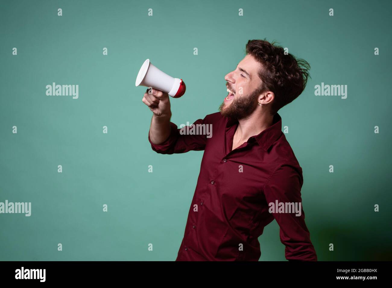 Bärtiger junger Mann, der in einem Megaphon laut redet. Konzept von Menschen, die ihre Stimme über die Menge hinaus erheben. Stockfoto