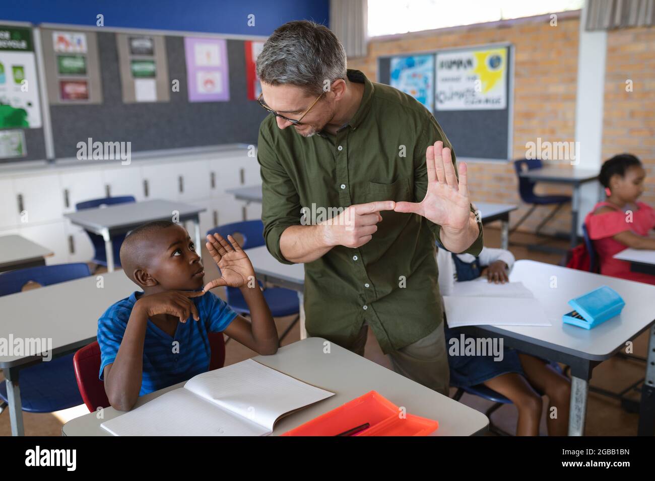 Kaukasischer Lehrer und afroamerikanischer Junge, der in der Hand spricht, signieren Sprache in der Schule Stockfoto