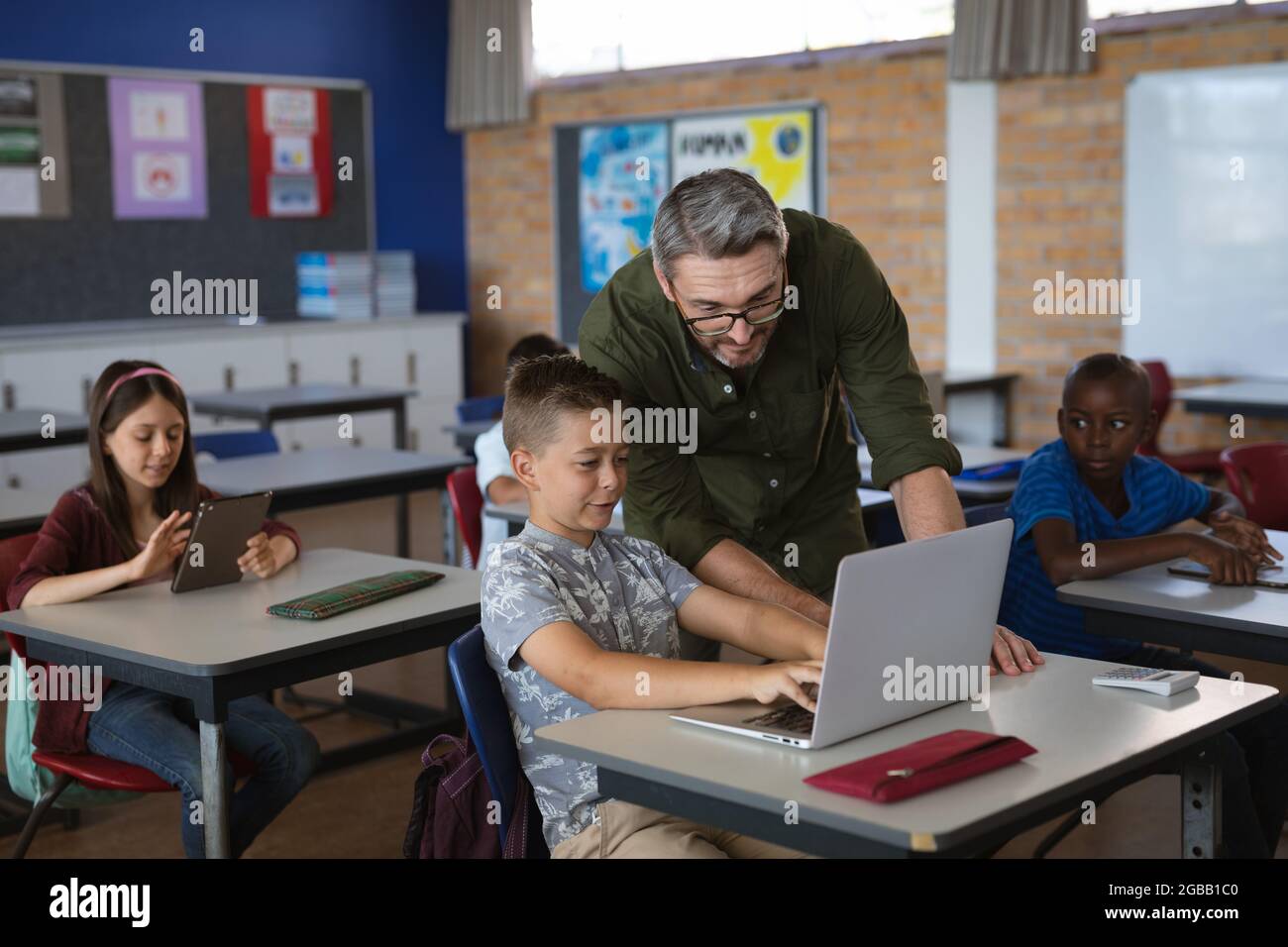 Kaukasischer männlicher Lehrer, der einem kaukasischen Jungen beibringt, wie er in der Schule in der Klasse einen Laptop benutzt Stockfoto