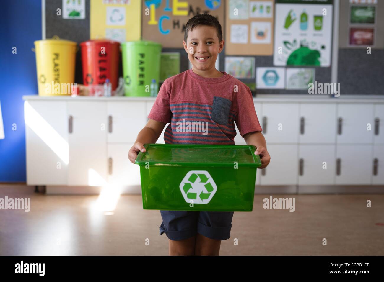 Porträt eines kaukasischen Jungen, der lächelt, während er in der Schule ein Tablett mit recycelbaren Plastikartikeln hält Stockfoto