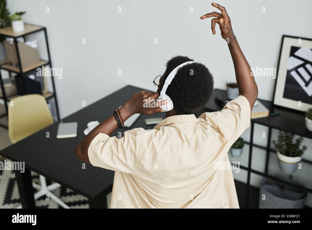 Rückansicht eines afrikanischen Mannes, der in kabellosen Kopfhörern Musik hört und in Büros tanzt Stockfoto