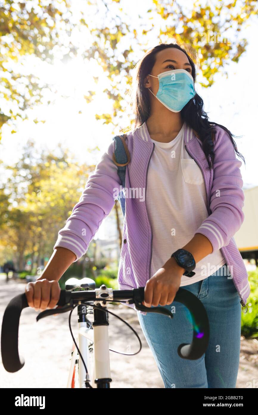 Asiatische Frau trägt Gesichtsmaske Wheeling Fahrrad im sonnigen Park  Stockfotografie - Alamy
