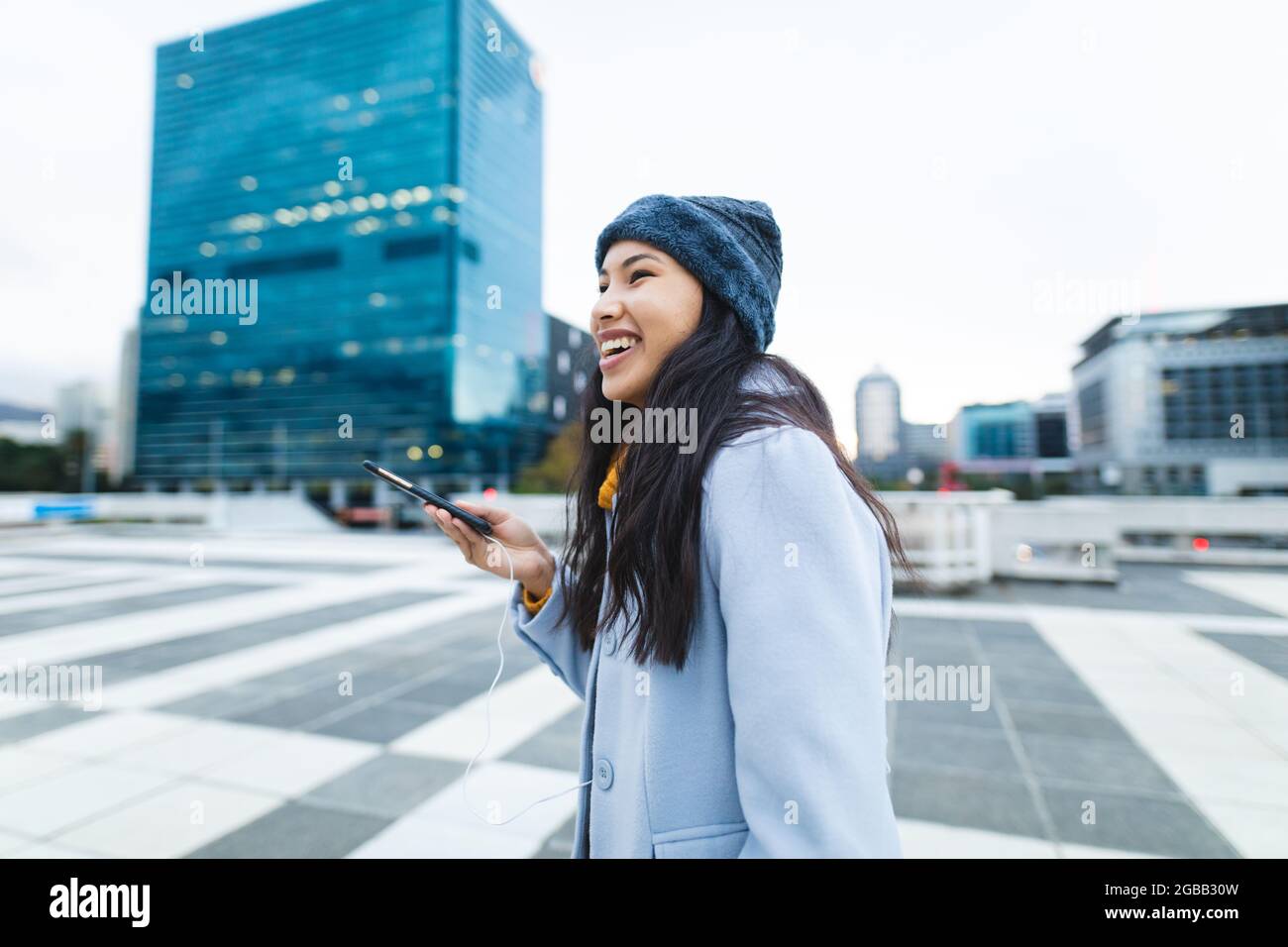 Asiatische Frau lächelt und benutzt Smartphone auf der Straße Stockfoto