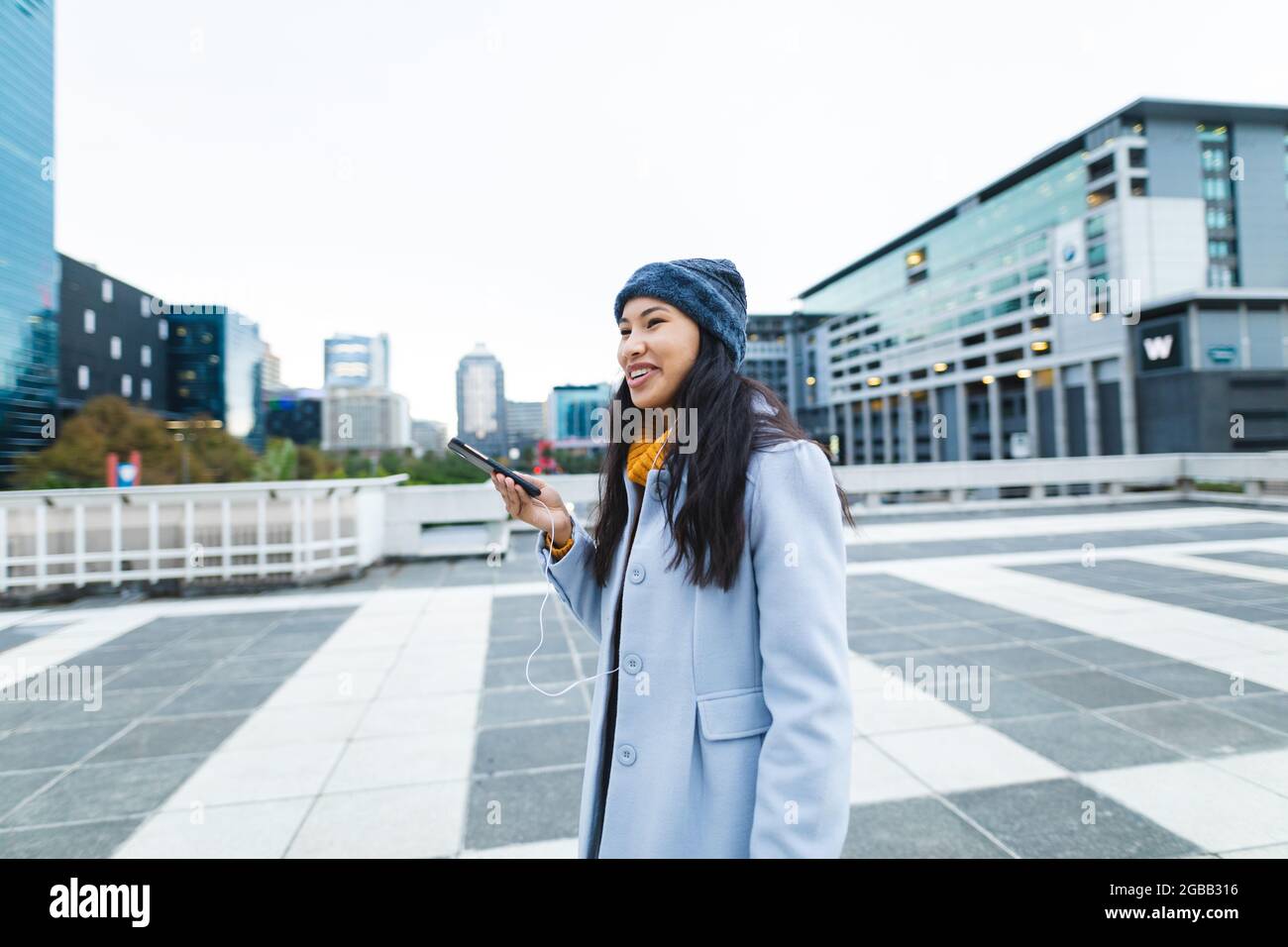 Asiatische Frau lächelt und benutzt Smartphone auf der Straße Stockfoto