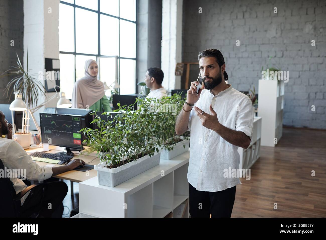 Junger seriöser muslimischer Geschäftsmann, der Kunden am Mobiltelefon im Arbeitsumfeld berät Stockfoto