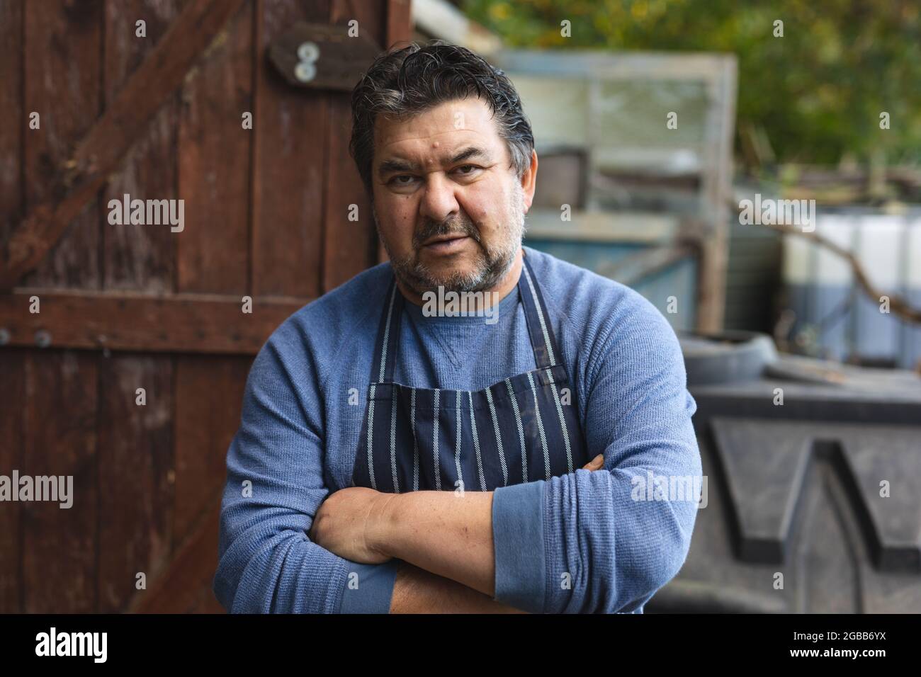 Porträt eines kaukasischen Gärtners mit gekreuzten Händen und Blick auf die Kamera in der Gartenmitte Stockfoto