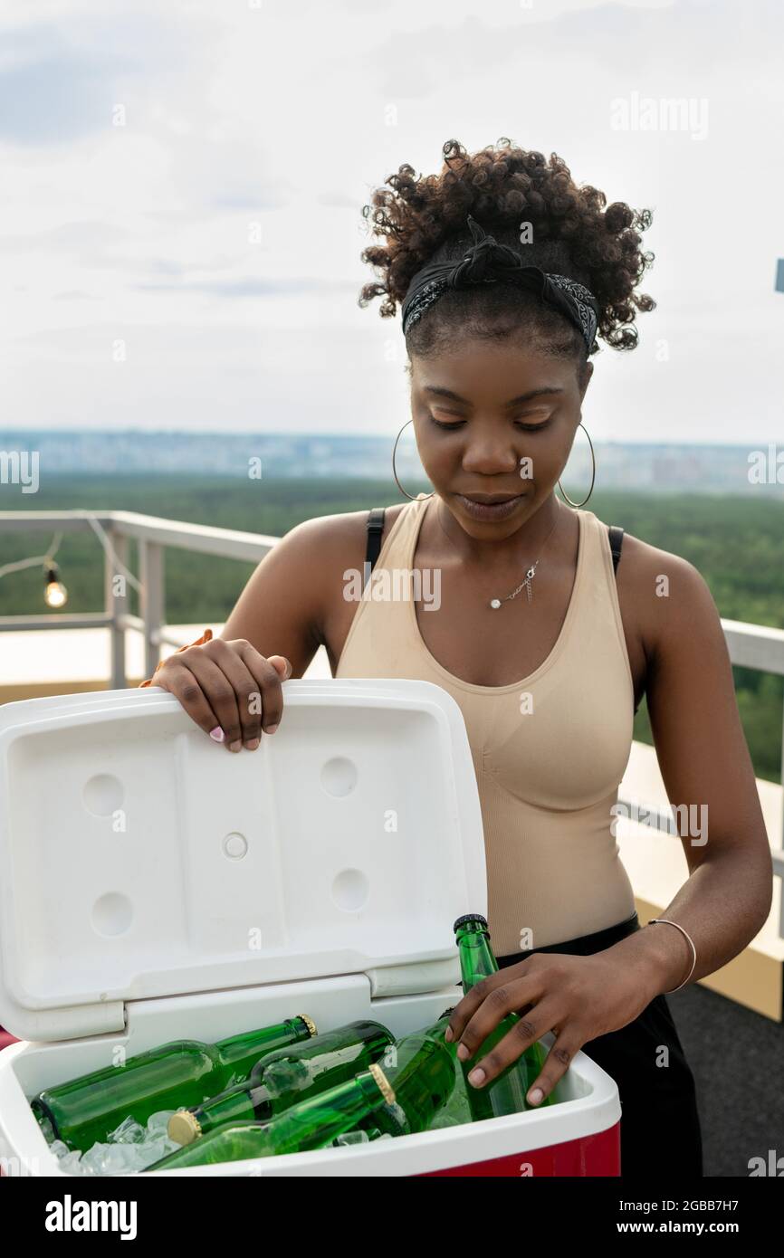 Junge hübsche Frau, die bei der Party im Café im Freien eine Flasche Bier mit Eiswürfeln aus dem Kasten nahm Stockfoto