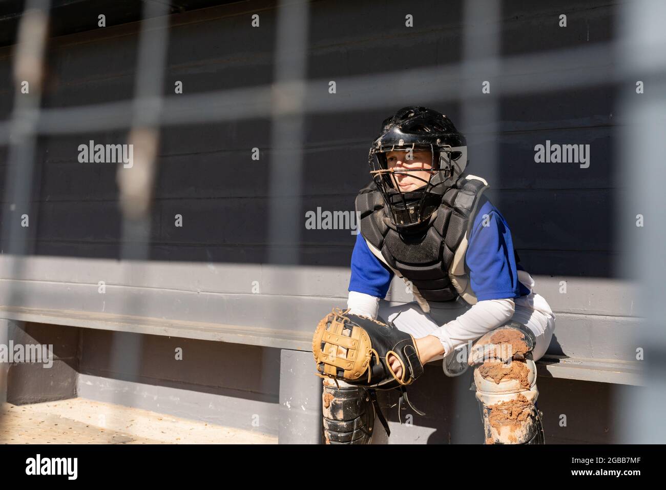 Kaukasische Baseballspielerin, die auf der Bank sitzt und Catcher's Helme und Schutzkleidung trägt Stockfoto