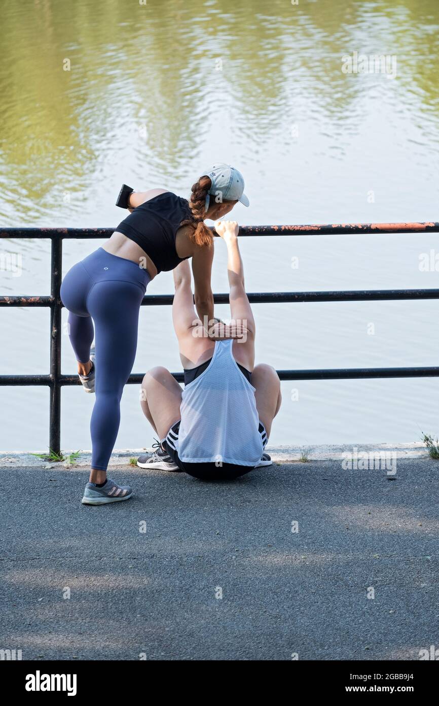 Ein sehr feingesspaßtes Personal Trainer führt einen Klienten durch tiefe Kniebeugeübungen in einem Park in Flushing, Queens, New York City. Stockfoto