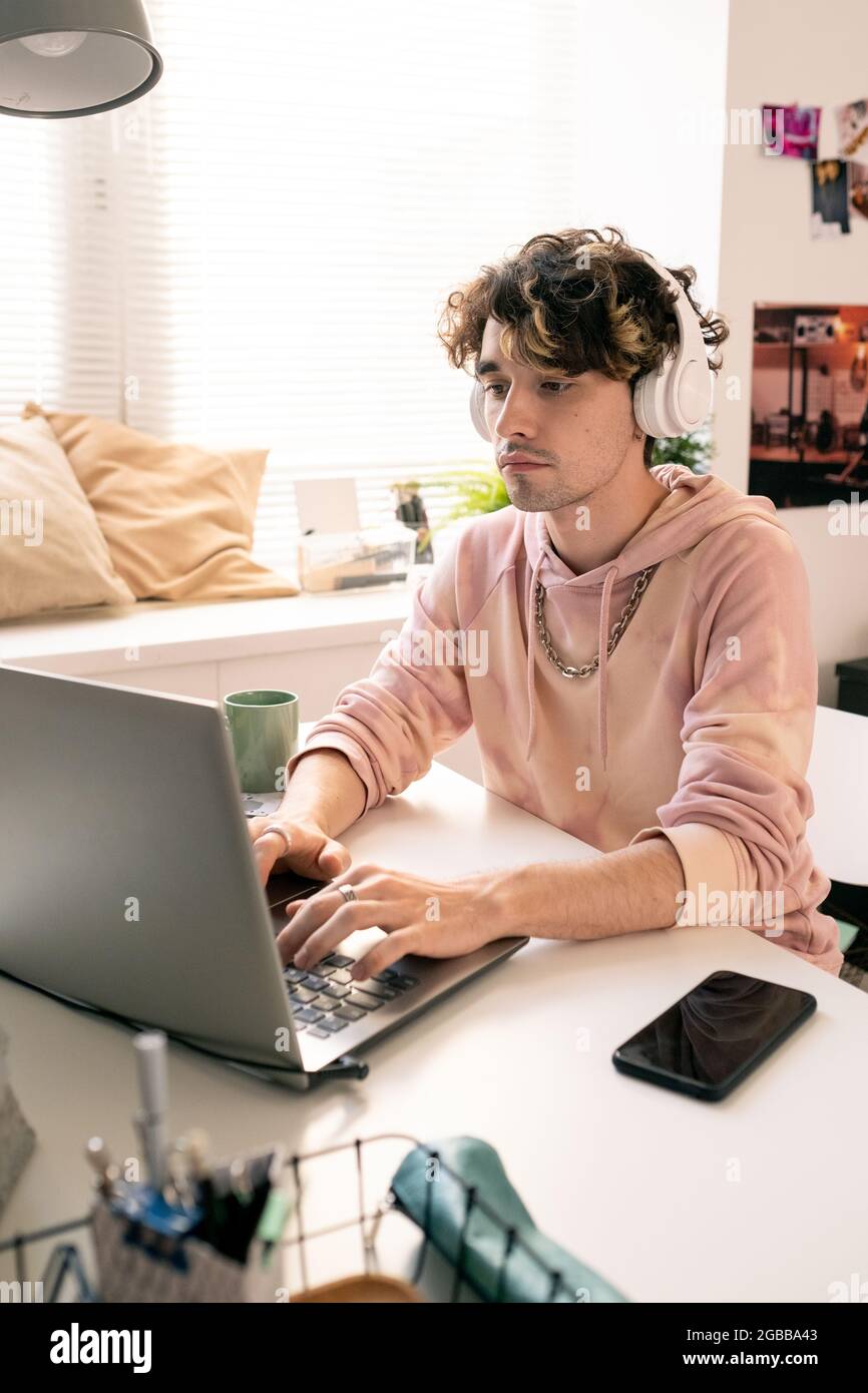 Moderner Typ mit Kopfhörern, der beim Tippen auf das Notebook-Display schaut Stockfoto