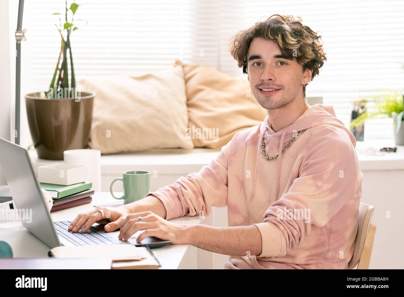 Fröhlicher Teenager mit Laptop, der während des Netzwerks mit einem Lächeln auf die Kamera blickt Stockfoto