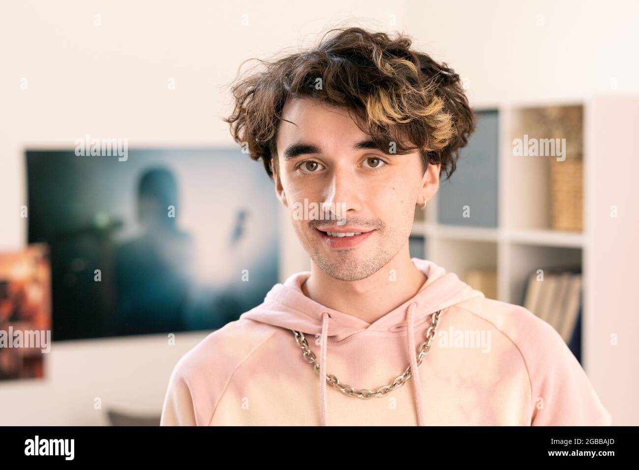 Moderner Teenager mit pinkem Hoodie und Blick auf die Kamera in der häuslichen Umgebung Stockfoto