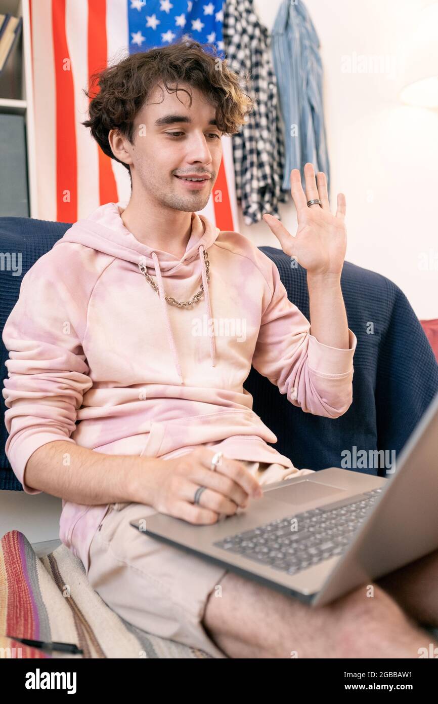 Glücklicher Teenager, der während der Online-Kommunikation vor dem Laptop die Hand an jemanden winkt Stockfoto