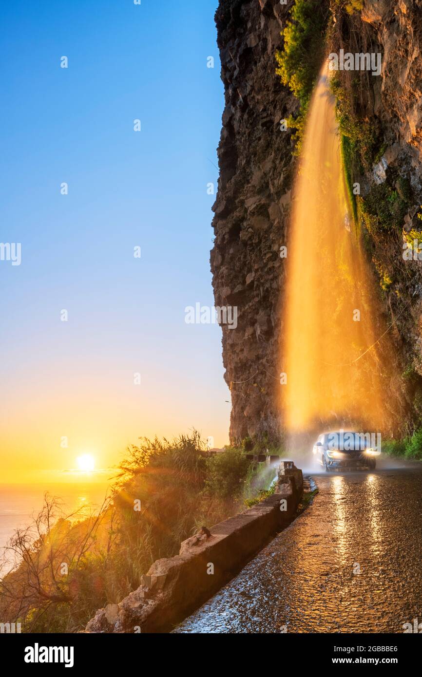 Auto, das bei Sonnenuntergang unter dem Wasserfall Anjos auf einer rutschigen Küstenstraße vorbeifährt, Ponta do Sol, Insel Madeira, Portugal, Atlantik, Europa Stockfoto