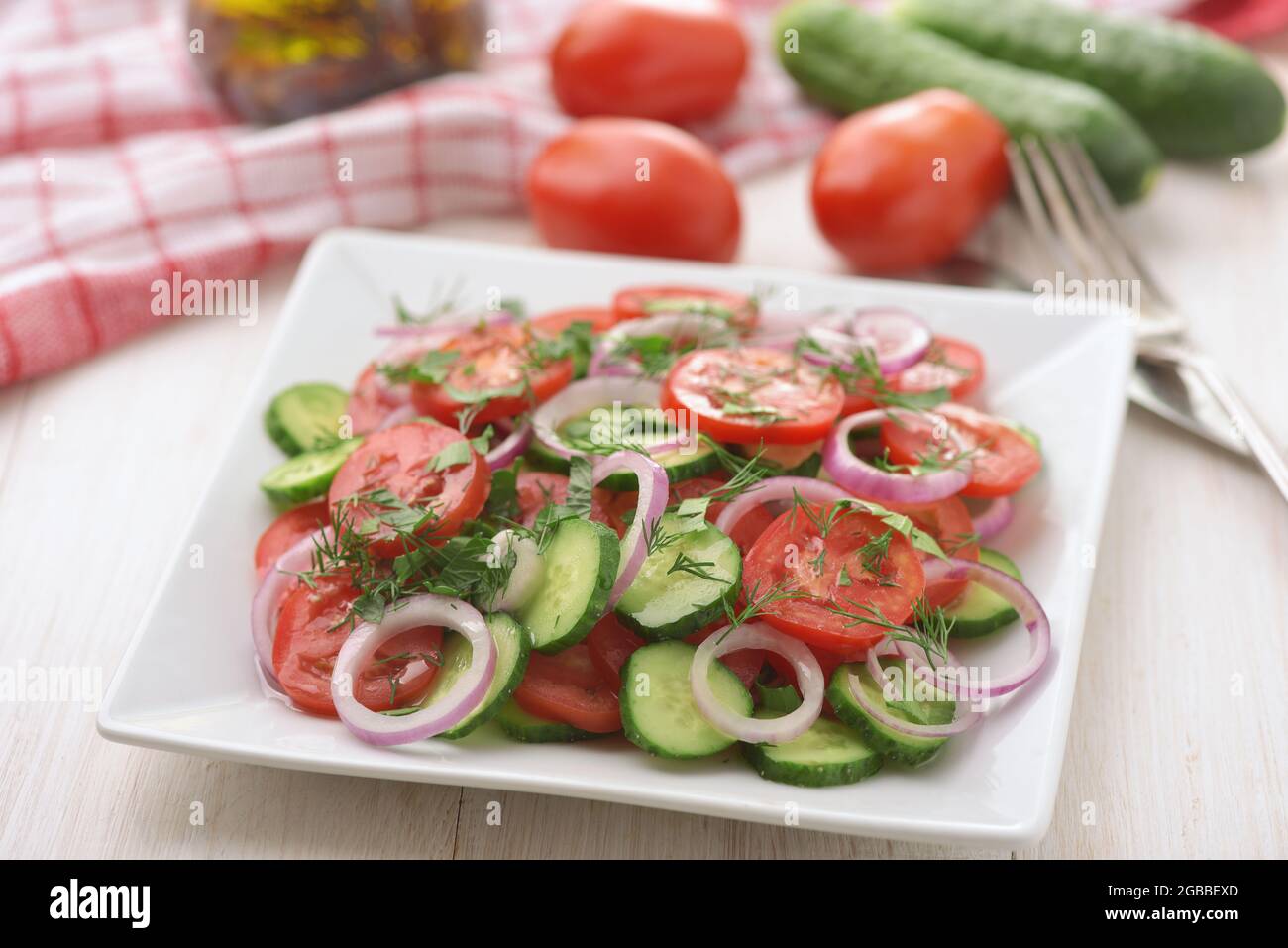 Frischer vegetarischer Gemüsesalat mit Gurke, Tomaten und roten Zwiebeln auf weißem Holztisch Stockfoto