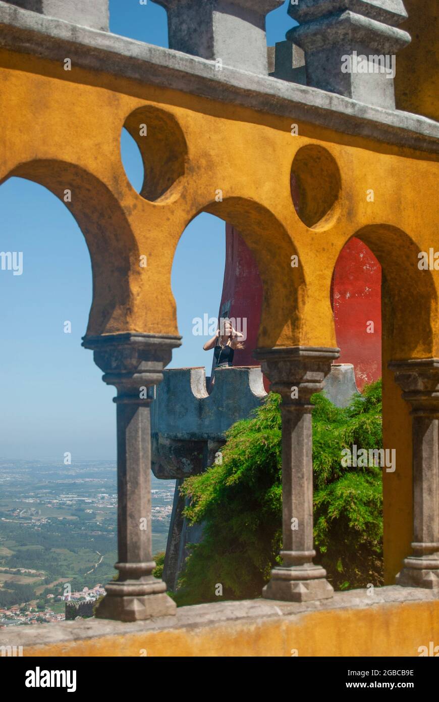 Eine Frau auf dem Balkon des Pena Palace, gelbe bögen im maurischen Stil im Vordergrund, wunderschöne Aussicht im Hintergrund Stockfoto