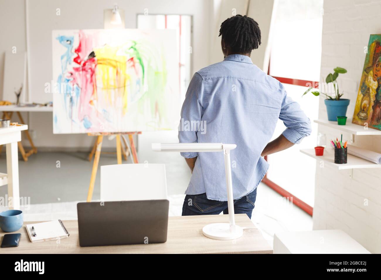 afroamerikanischer Maler bei der Arbeit beim Betrachen von Kunstwerken im Kunststudio Stockfoto