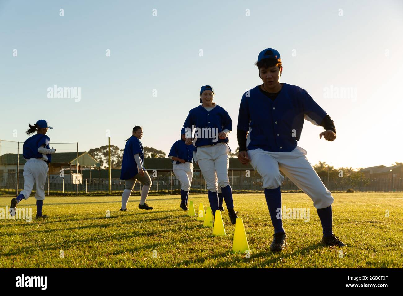 Verschiedene Baseballspielerinnen, die sich bei Sonnenaufgang auf dem Spielfeld aufwärmen und Slalom um Kegel laufen Stockfoto