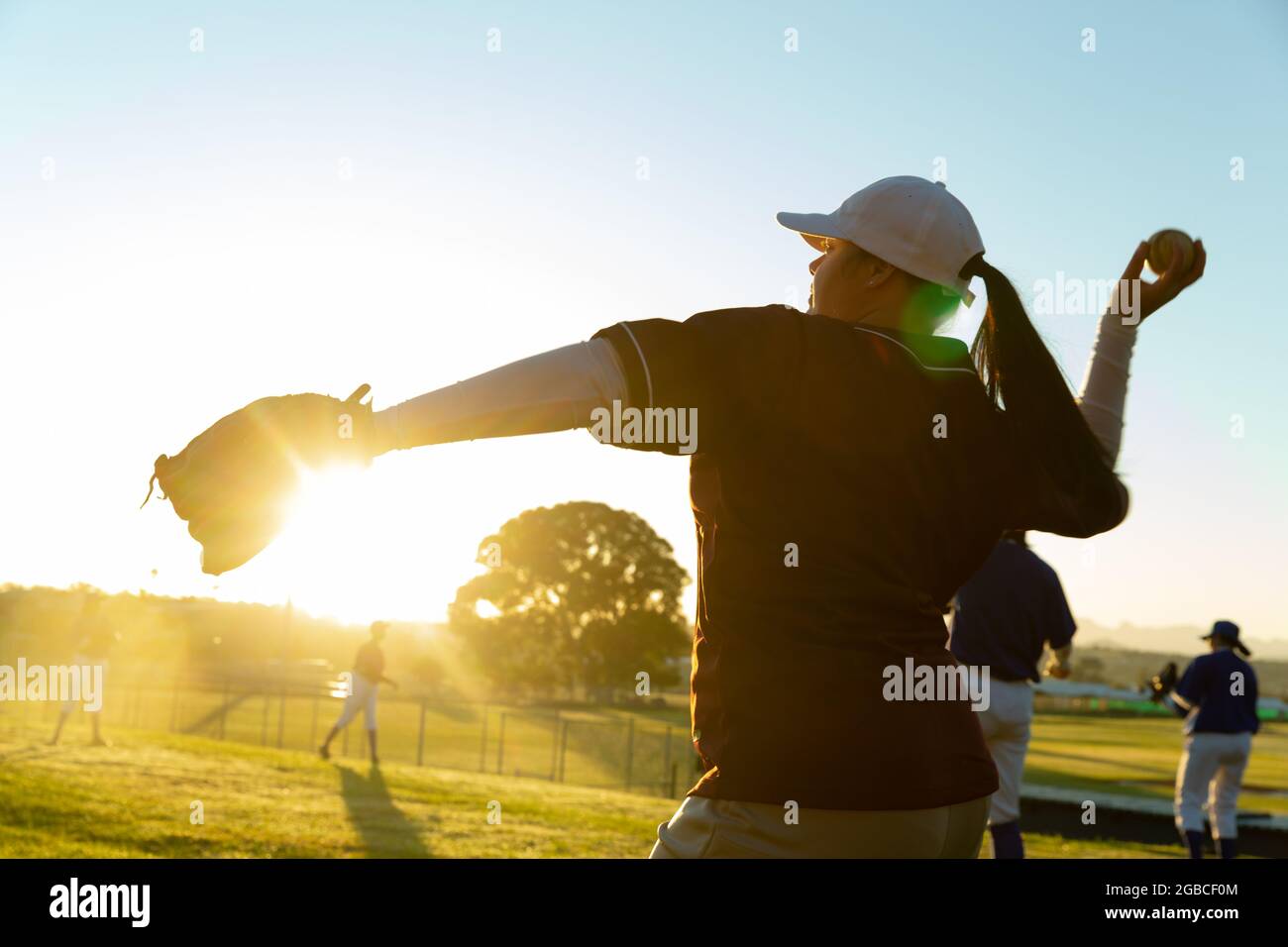 Verschiedene Gruppen von Baseballspielerinnen, die sich bei Sonnenaufgang auf dem Spielfeld aufwärmen, Kugeln werfen und fangen Stockfoto