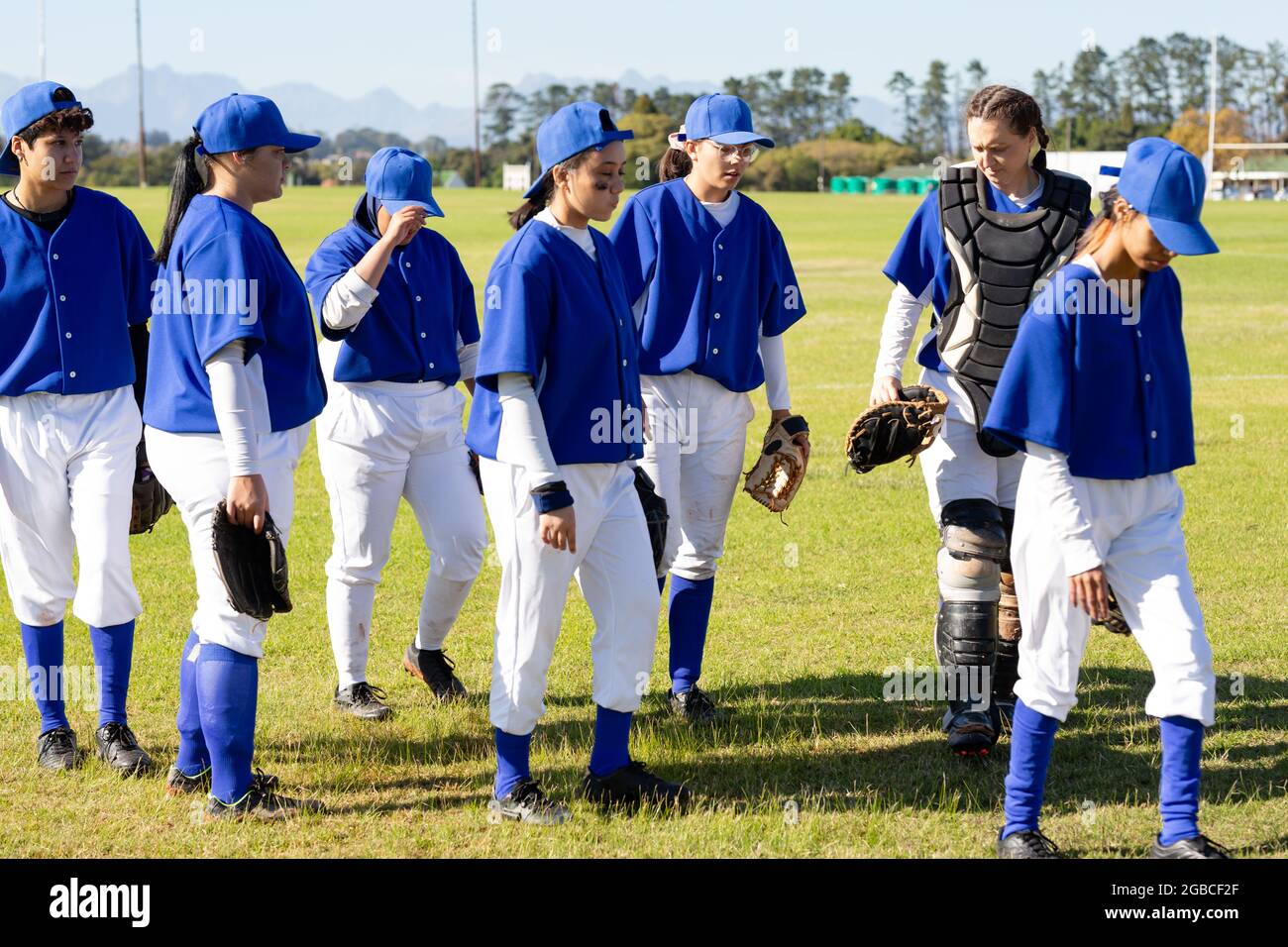 Eine vielfältige Gruppe weiblicher Baseballspieler, die nach dem Spiel vom sonnigen Baseballfeld aus spazieren gehen Stockfoto