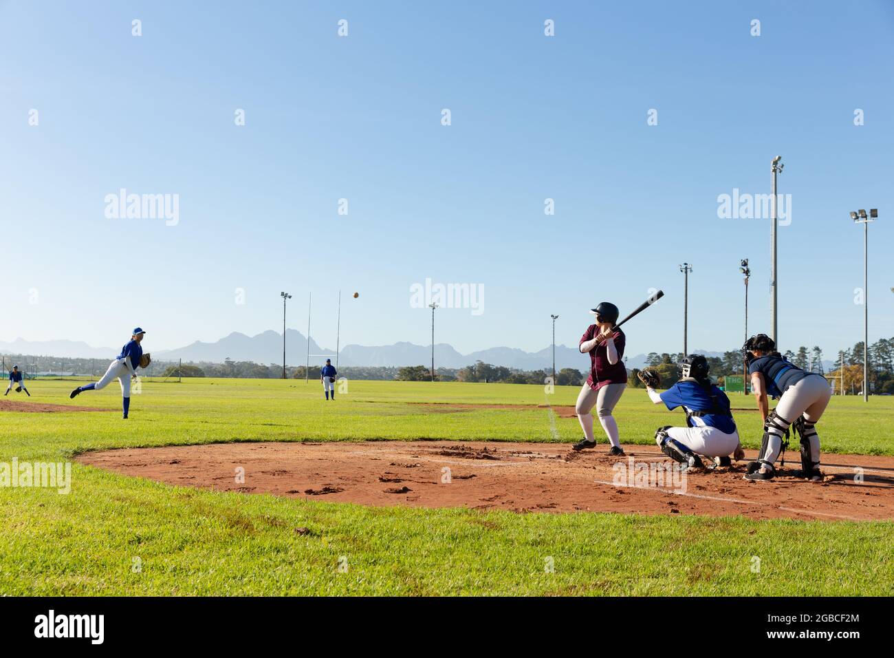 Verschiedene Baseballspielerinnen in Aktion auf sonnigem Baseballfeld während des Spiels Stockfoto