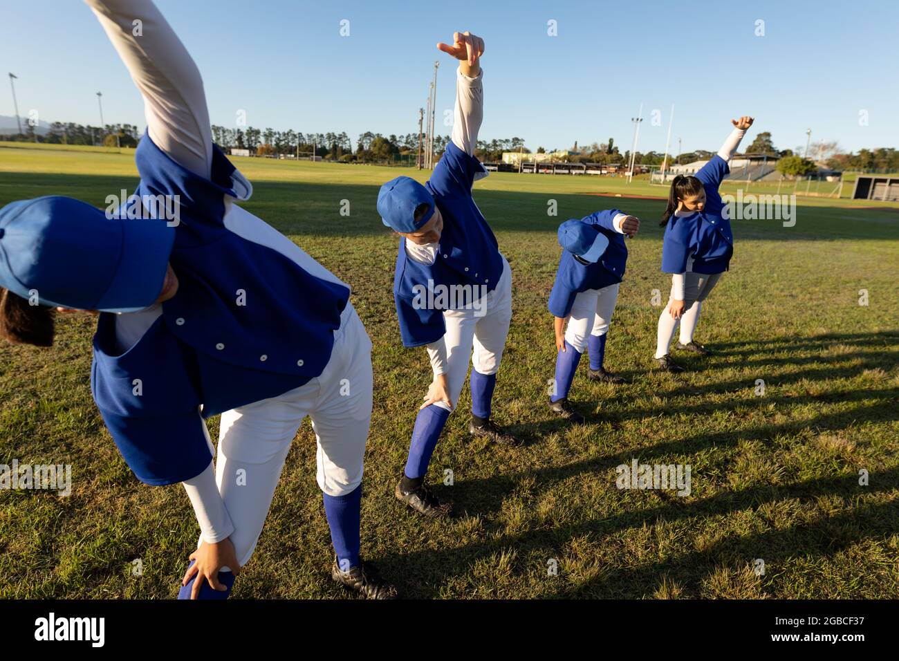 Verschiedene Gruppen von Baseballspielerinnen, die sich auf dem Spielfeld aufwärmen und sich von der Hüfte ausstrecken Stockfoto