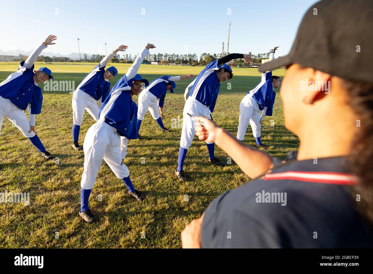 Verschiedene Baseballspielerinnen mit Trainer, die sich auf dem Spielfeld aufwärmen und sich von der Hüfte ausstrecken Stockfoto