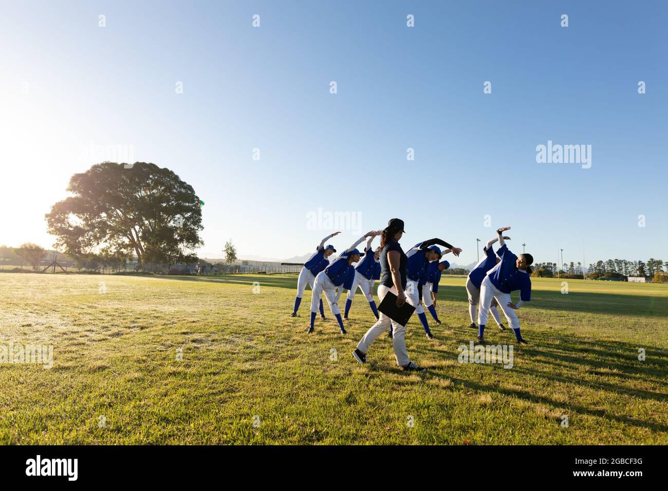 Verschiedene Baseballspielerinnen mit Trainer, die sich im Feld von der Hüfte aus aufwärmen Stockfoto