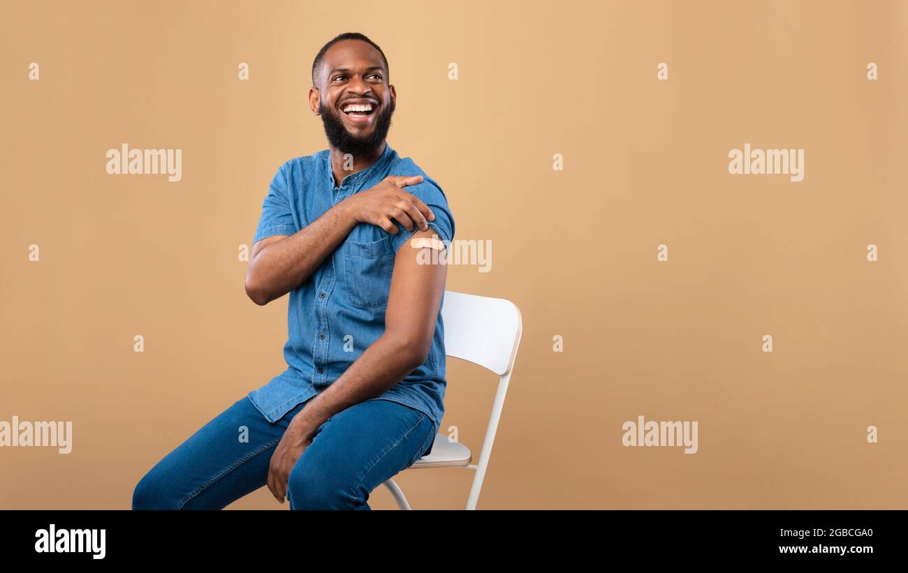 Coronavirus-Impfung rettet Leben Banner. Fröhlicher schwarzer Mann posiert mit Bandhilfe am Arm, nachdem er einen kovidierten Impfstoff erhalten hat Stockfoto