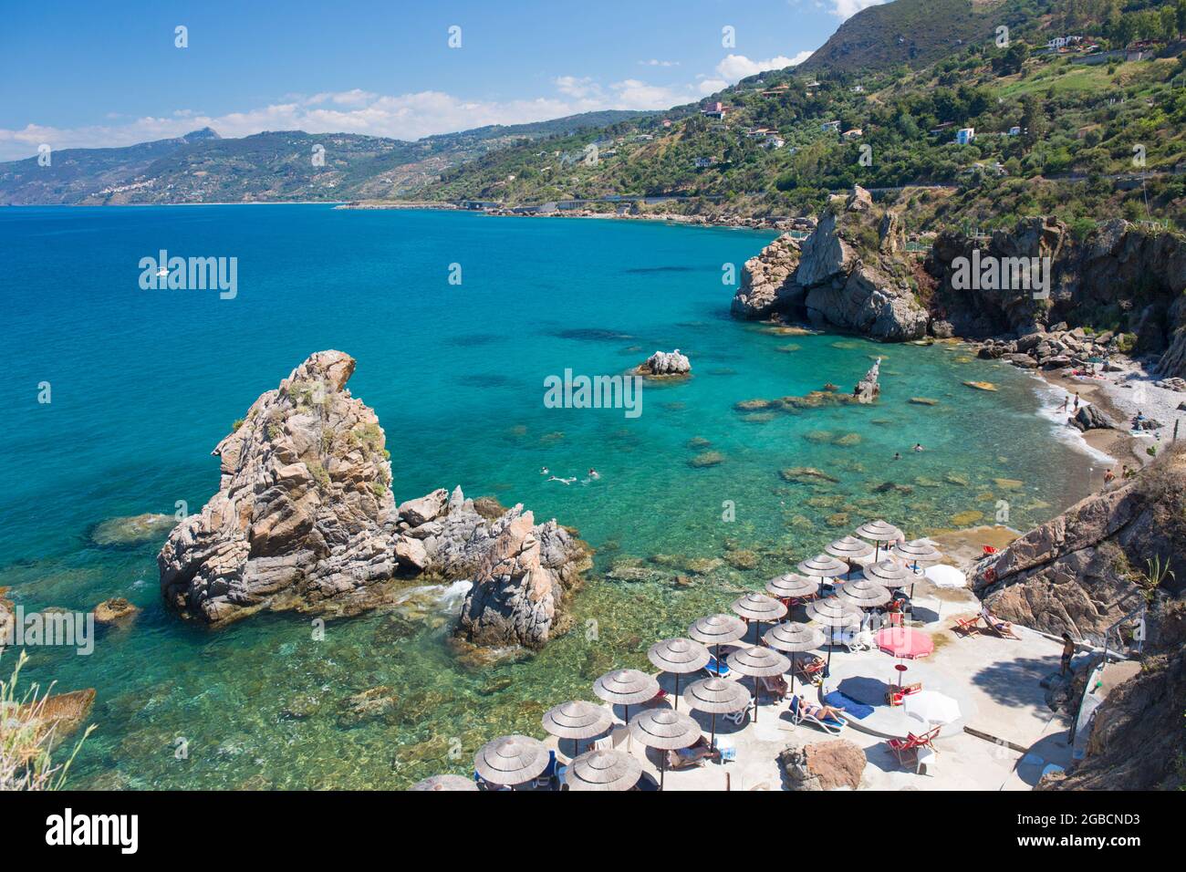 Cefalù, Palermo, Sizilien, Italien. Blick über das klare türkisfarbene Wasser der Calura Bay, Touristen entspannen sich unter Sonnenschirmen am Strand. Stockfoto