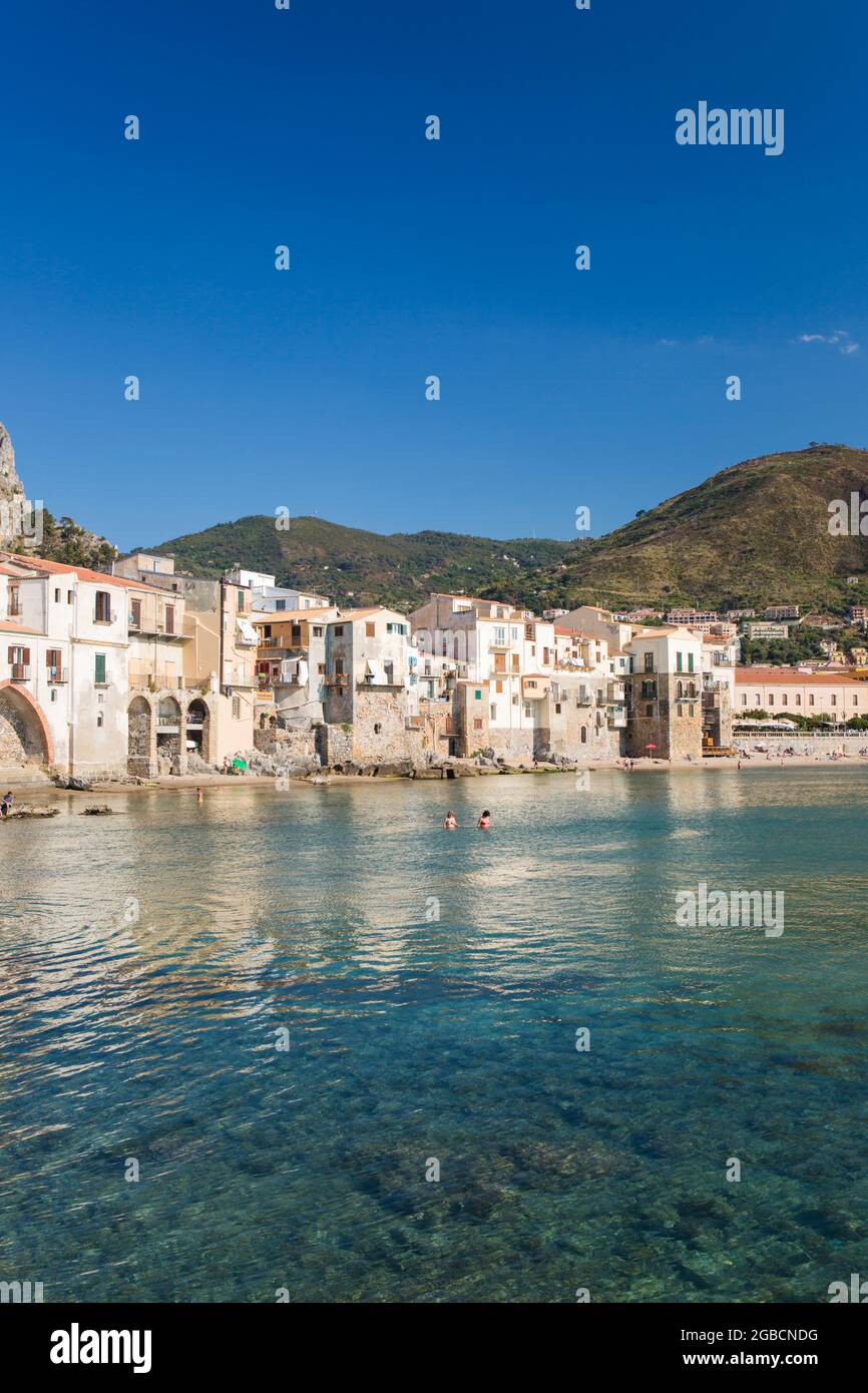Cefalù, Palermo, Sizilien, Italien. Blick über den ruhigen Hafen auf die Altstadt, überhängende Häuser, die sich entlang der Uferpromenade gruppieren. Stockfoto