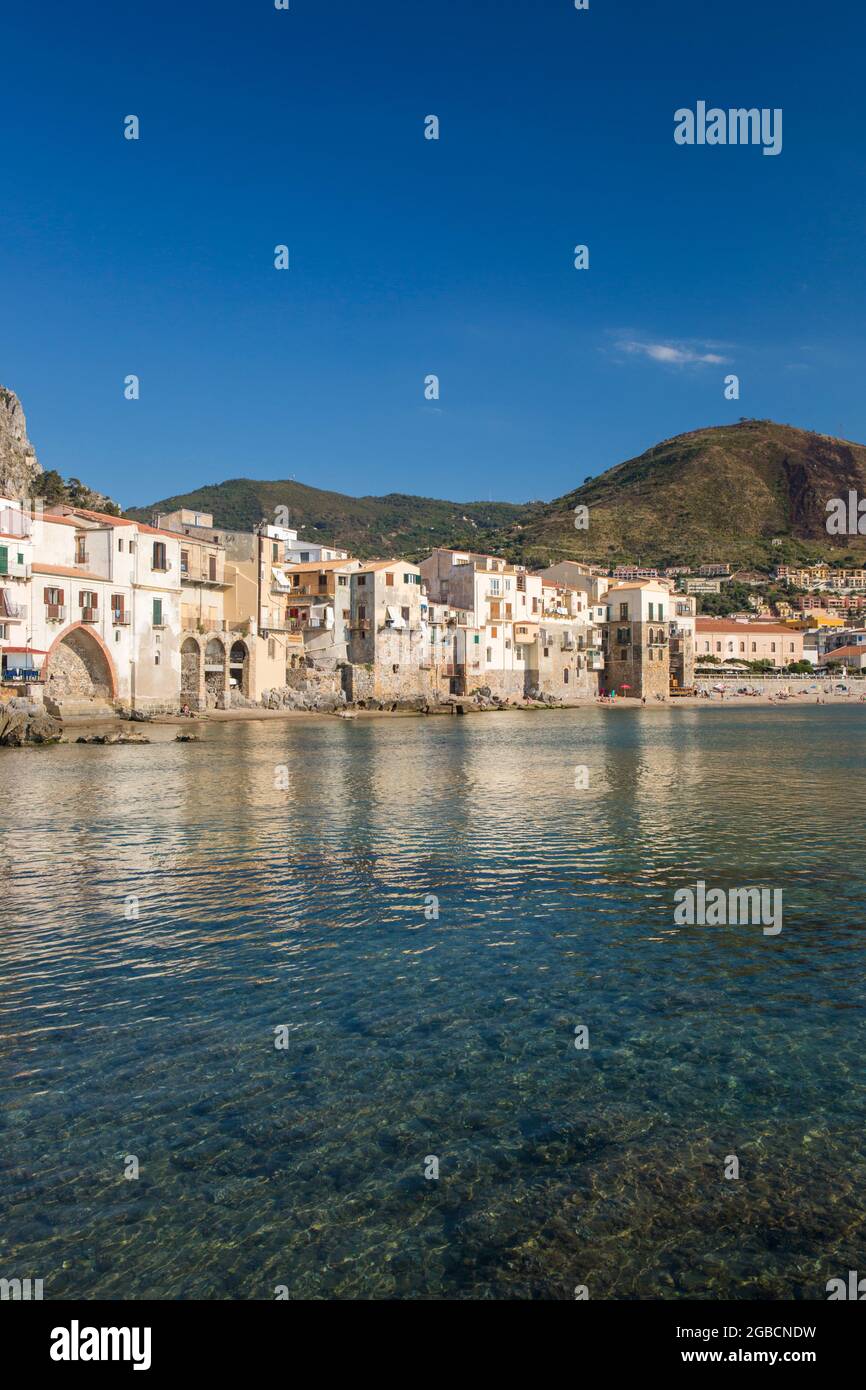 Cefalù, Palermo, Sizilien, Italien. Blick über den ruhigen Hafen auf die Altstadt, überhängende Häuser, die sich entlang der Uferpromenade gruppieren. Stockfoto