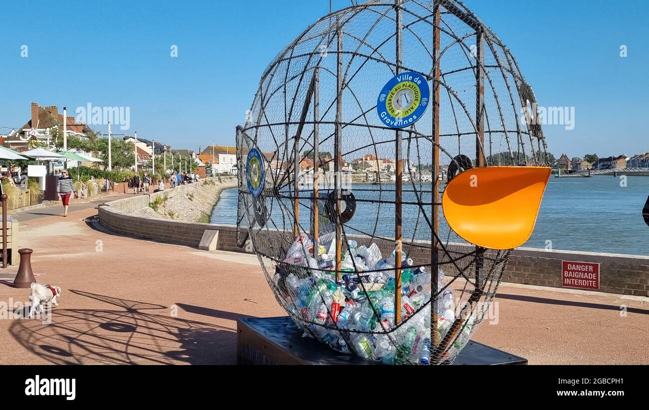 Lustige Mülltonne in Form eines Fischs, der Plastikmüll schluckt, an der Promenade am Seeufer in der Stadt. Sign in French: 'swimming forbidden'. Stockfoto
