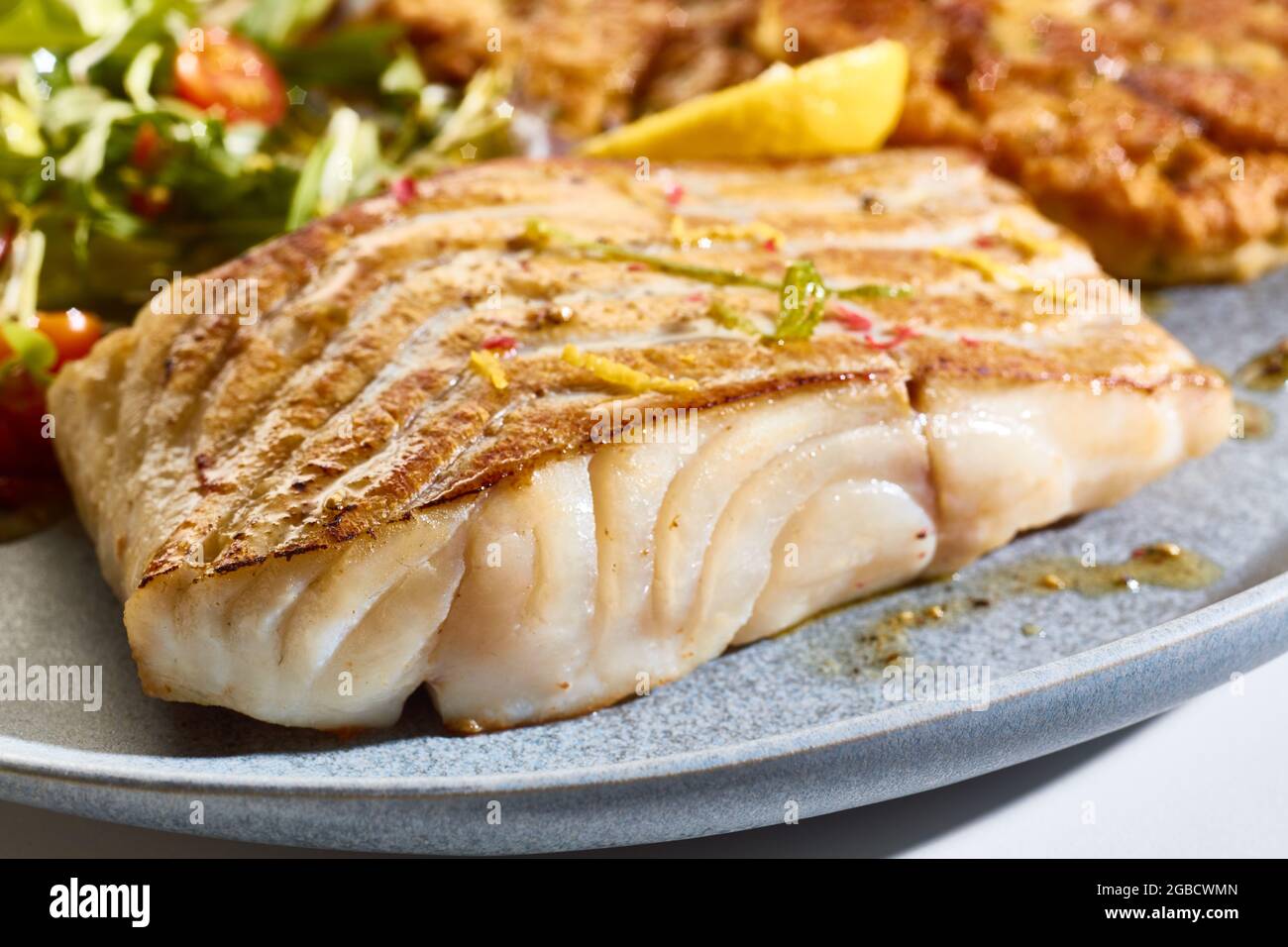 Appetitliches, frisch gebackenes Pollack-Fischsteak auf dem Teller mit gemischten Salatblättern und Zitrone Stockfoto