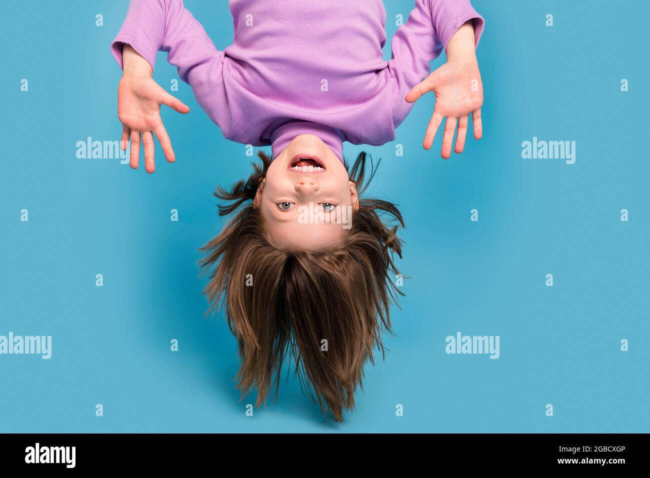 Portrait Foto kleines Mädchen hängend auf dem Kopf nach unten isoliert pastellblau Hintergrund Stockfoto