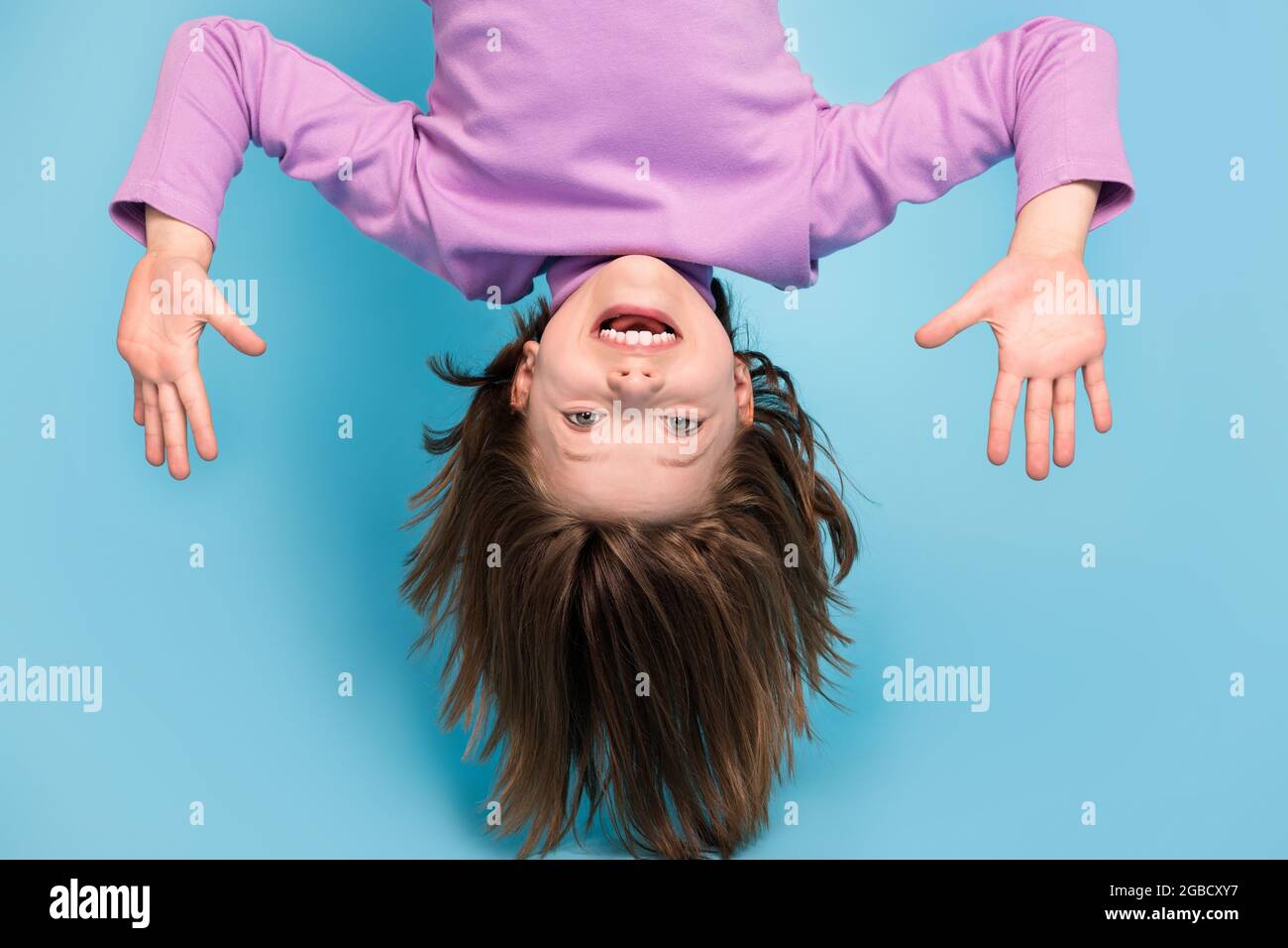 Portrait Foto kleines Mädchen hängend auf dem Kopf lachend überglücklich isoliert pastellblau Hintergrund Stockfoto