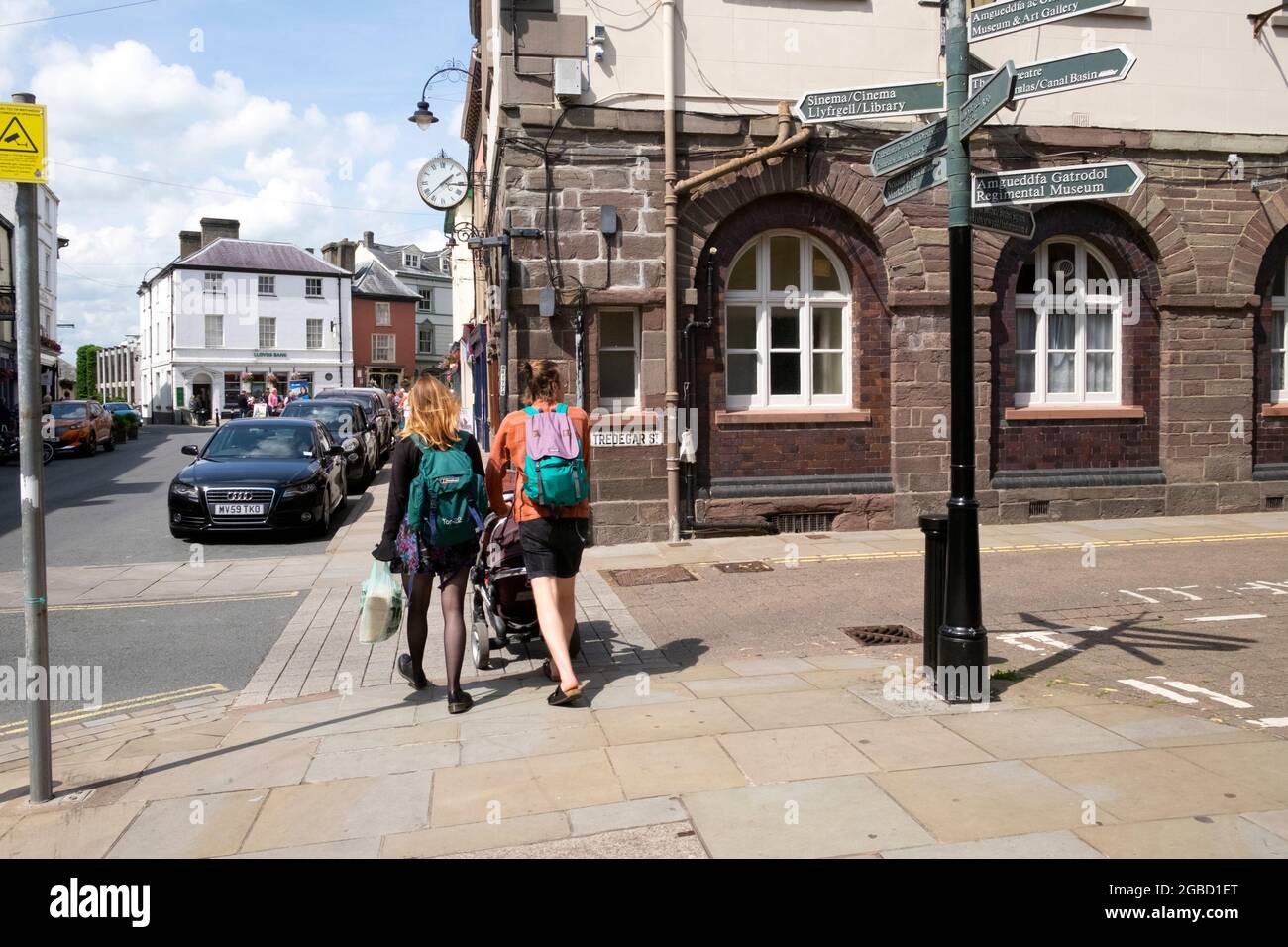 Rückansicht eines jungen Paares mit Rucksäcken, das einen Kinderwagen auf der Hauptstraße im Stadtzentrum von Brecon schiebt Sommer 2021 Powys Wales Großbritannien KATHY DEWITT Stockfoto
