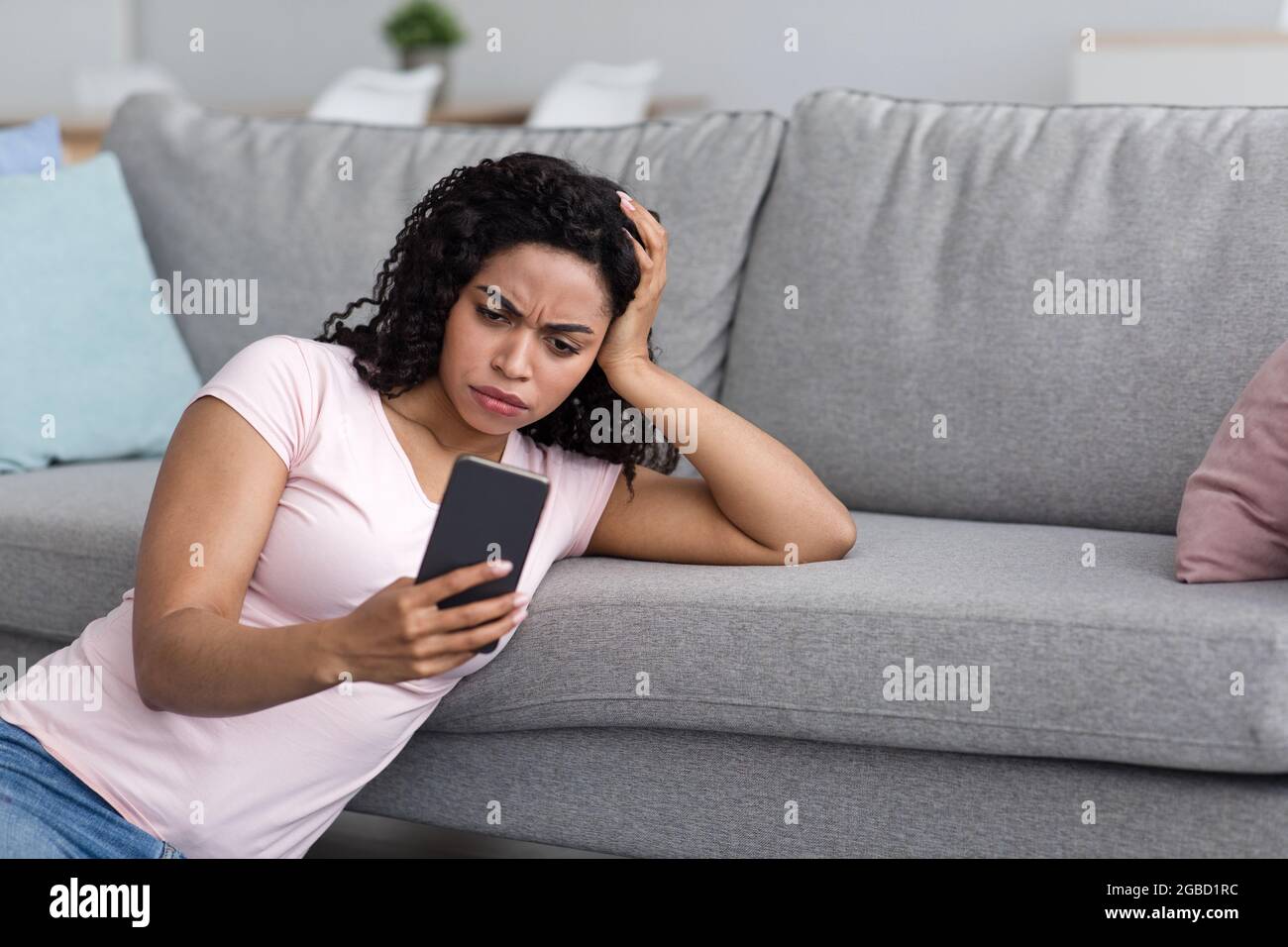 Frau verärgert nach dem Lesen der schlechten Nachricht am Telefon zu Hause Stockfoto