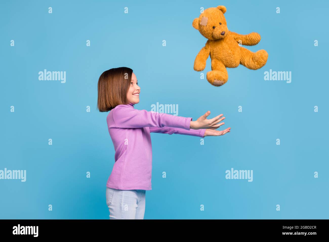 Foto von niedlichen süßen Schulmädchen tragen lila Rollkragen fangen braun Teddybär lächelnd isoliert blaue Farbe Hintergrund Stockfoto