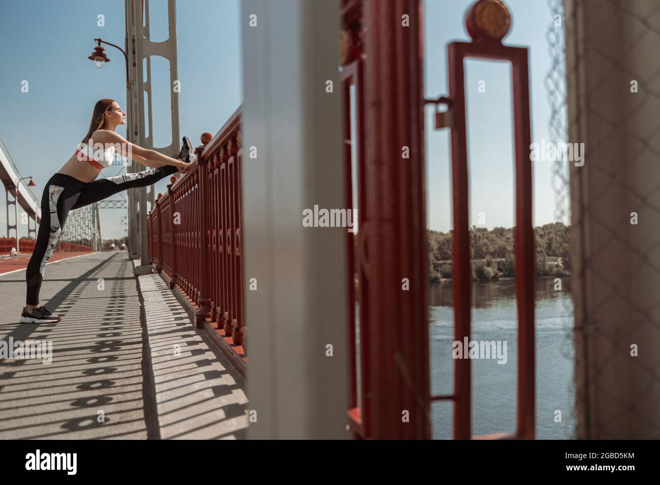 Konzentrierte kurzhaarige Frau macht Dehnungsübungen auf einer zeitgenössischen Brücke Stockfoto