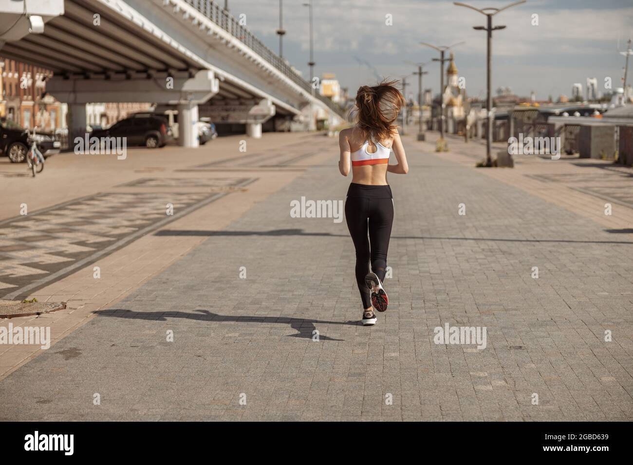 Frau im Trainingsanzug mit lockeren Haaren läuft entlang leerer Stadtpromenade Stockfoto